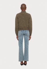 Pull en tricot marron et crème, col montant, manches et ourlet côtelés. Associé à un jean flare bleu clair et des sandales à talons noires.
