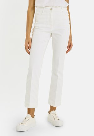 Pantalones blancos ajustados, recortados, con bolsillos delanteros y cierre de botón, combinados con zapatillas blancas de plataforma.