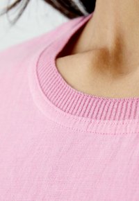 Hellrosa Sweatshirt mit Rundhalsausschnitt, ribbeligem Kragen und glatter Stoffoberfläche. Das Bild konzentriert sich auf den Kragen- und Schulterbereich.