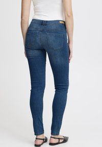 Vaqueros ajustados de mezclilla azul oscuro, diseño de talle alto, con dos bolsillos traseros y una etiqueta de cuero sutil en la pretina.