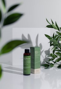 Grönt te-ansiktsvatten i en genomskinlig flaska med svart kork. Lådan har gröna och krämfärgade detaljer, utförlig text och en slät finish.