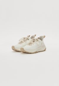 Lettvekts atletisk sko i off-white med beige detaljer, med en teksturert overdel, snøring og en robust, grepfokusert såle.