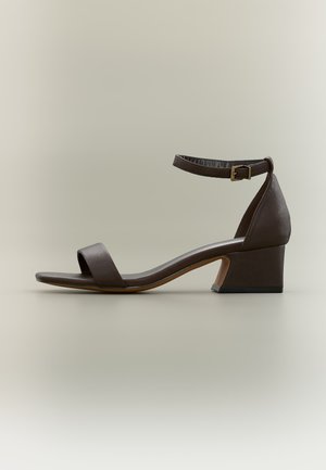 Dark brown low block heel sandal with ankle strap and front toe strap on a neutral background.