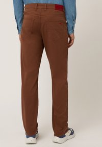 Pantaloni di cotone marrone con taglio dritto, dotati di due tasche posteriori e un piccolo logo del marchio rosso vicino alla vita.