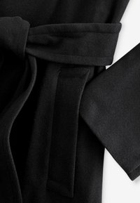 Rochie de pluș neagră cu un cordon legat, având o textură netedă și mâneci largi, cu un design minimalist și detalii de buzunare ascunse.