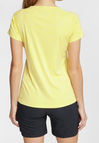 Żółta koszulka z krótkim rękawem o subtelnym paskowanym wzorze, zestawiona z ciemnymi szortami. Koszulka ma okrągły dekolt i luźny krój.