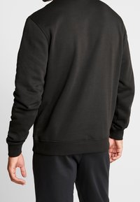 Felpa nera con collo rotondo e polsini a coste, realizzata in stoffa morbida. Presenta una texture liscia e un design svasato.