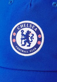 Blå baseballcaps med et broderet rundt Chelsea Football Club-logo med en løve, omgivet af røde accenter og tekst.
