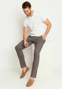 Biała koszulka polo z krótkim rękawem, szare spodnie slim-fit i jasnobrązowe mokasyny. Gładka tekstura, casualowy design i luźny krój.