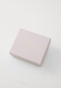 Scatola quadrata rosa con una texture liscia, presenta la scritta dorata "Coccinelle" centrata sulla superficie superiore. Design semplice e minimalista.