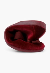 Zapato de terciopelo rojo con una textura suave, forma redondeada y un detalle de cinta en el interior. Suela plana y borde exterior ligeramente endurecido.