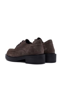 Brown suede shoes with a round toe, featuring black laces, a smooth back, and chunky black rubber soles. Low-cut design.