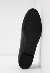 Semelle de chaussure en cuir noir avec petit talon, taille 4½, nom de marque "högI" visible sur la semelle, positionnée verticalement contre un coin blanc.