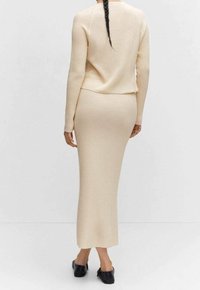 Beige ribbed knit sweater ja hame yhdistelmä, vartalonmyötäinen siluetti, tekstuuri kangas, pitkät hihat, lattiahame, yhdistetty mustien kenkien kanssa.