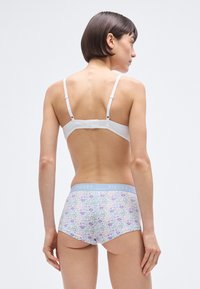 Bela modrček z nastavljivimi trakovi, kombiniran z boyshort hlačkami s cvetličnim potiskom, ki imajo svetlo modro pasno obrobo z napisom "PIECES".