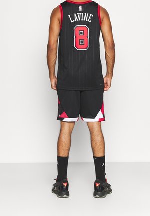 Homme debout de dos portant un maillot de basket noir avec "LAVINE" et le numéro 8, un short noir, des chaussettes noires et des baskets.