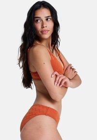 Ensemble bikini orange avec un motif texturé en zigzag. Comprend un haut triangulaire à fines bretelles et un bas taille basse.