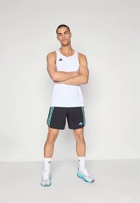 Valge lühikeste varrukateta spordipluus, mustad lühikesed püksid türkiissiniste triipudega, seljas valged sokid ja jooksujalatsid. Lihtne sportlik disain, ilma mustriteta.