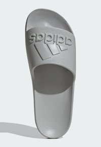 Šedá skluzná sandála s texturovaným povrchem. Obsahuje velké logo a design tří pruhů přes horní pásek. Měkká, tvarovaná stélka.