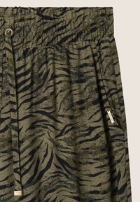 Pantalones de tela verde con un estampado de rayas de tigre en negro y verde oscuro, cinturilla elástica, cordón y bolsillo lateral con etiqueta de la marca.