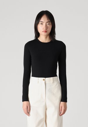 Bodysuit negro de manga larga con escote redondo, diseño ajustado, usado con pantalones blancos de cintura alta con cierre de botón.