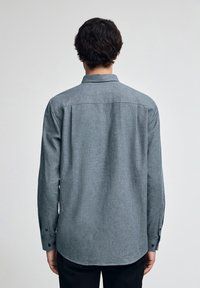 Grå skjorta med lång ärm, spetsig krage och subtil struktur. Avslutad med svarta knappar och rundad nederkant.