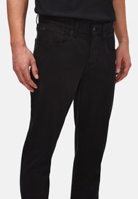 Sorte denim jeans med slim fit, der har forlommer, knaplukning og en glat tekstur. Skræddersyet design med minimal detaljering.