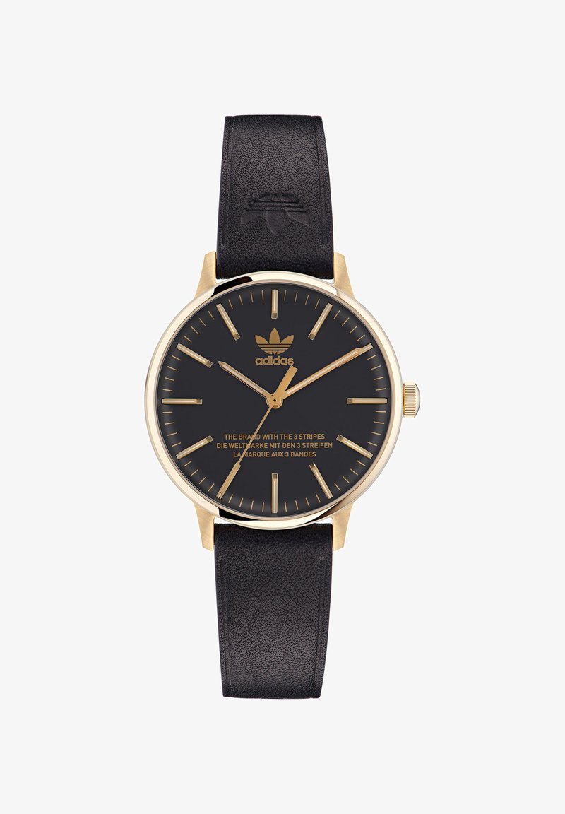 Zlata okrogla ura z črnim številčnikom in zlatimi urnimi oznakami. Črn usnjen pas z vtisnjenim logotipom. Vsebuje blagovno znamko v zlatem.