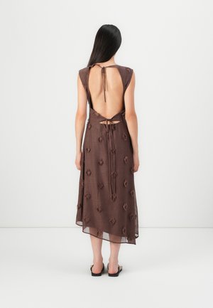 Brun, sans ermer, kjole med åpen rygg, knytefeste og teksturerte blomsterdetaljer overalt. Stoffet ser lett og flytende ut.