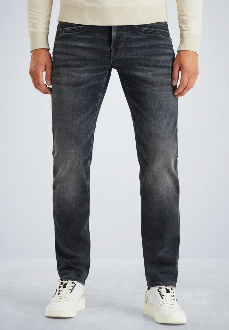 Tamno sivi traperice uskog kroja. Imaju suptilno izbjeljivanje, klasičan dizajn s pet džepova i vidljive detalje šavova. U kombinaciji s bijelim tenisicama.