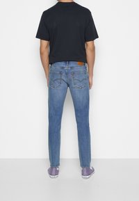 Modré džíny z denimu s přímo střiženým střihem, obsahující zadní kapsy s detaily švů a hnědou koženou nášivkou na pásku.