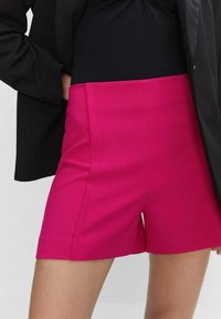 Fuchsia hoge taille shorts met een getailleerde pasvorm, een soepele textuur en zijzakken. Gecombineerd met een zwart topje en een donkere jas.