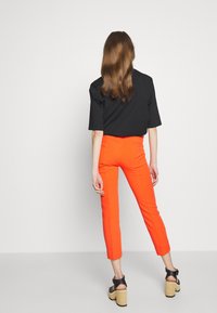 Haut noir à manches courtes associé à un pantalon orange slim taille haute et des sandales plateformes noires épaisses. Tissu lisse, silhouette moderne.