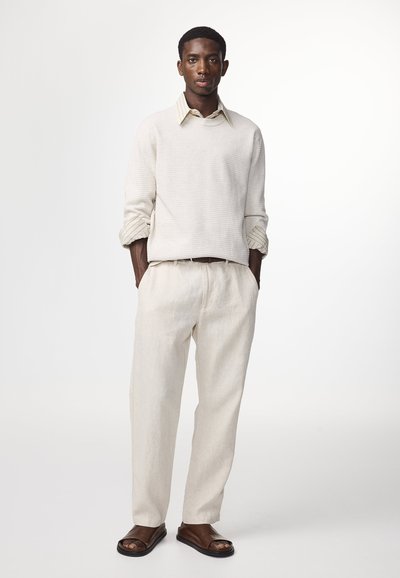 Lys beige sweater med ribbet tekstur, lagt over en stribet skjorte. Afslappet pasform lette linnedbukser og brune slip-on sandaler.