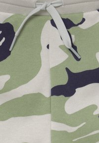 Bomullsshorts med ett camouflagemönster i grön, marinblå och vit. Har en elastisk midja med en ljusgrå dragsnöre.