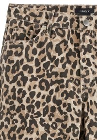 Le tissu en jean à motif léopard présente un fond beige avec des taches noires et marron foncé. Il comprend des poches et une fermeture à bouton visible.
