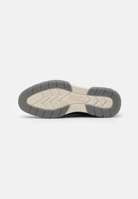 Black sneaker sole with light gray and cream accents, featuring a textured pattern, grooves for traction, and a brand logo.