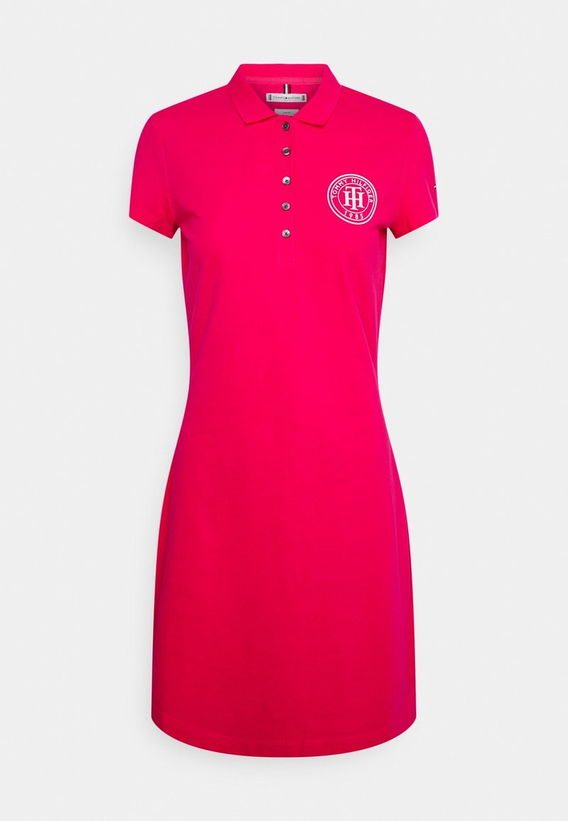 Robe polo à manches courtes rose vif avec cinq boutons et un logo circulaire Tommy Hilfiger sur le côté gauche de la poitrine.