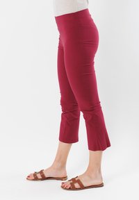 Pantaloni rossi alla caviglia con una trama liscia e una vita elasticizzata, caratterizzati da un orlo stretto. Abbinati a sandali scivolati marroni.