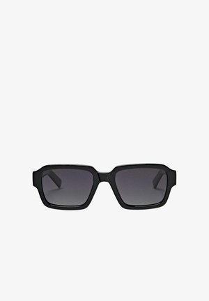 Schwarze rechteckige Sonnenbrille mit dicken Rahmen und dunkel getönten Gläsern vor weißem Hintergrund.