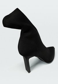 Chaussure à talon haut noire en tissu texturé, avec un bout pointu et un talon élégant et anguleux. Le design présente une silhouette drapée unique.
