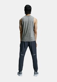 Šedý bezrukávový top doplněný černými cargo kalhotami s reflexními pruhy a elastickými manžetami. Sportovní boty dotvářejí celý outfit.