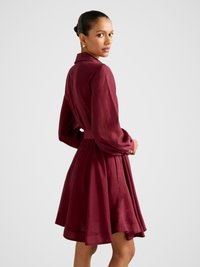 Bordové košeľové šaty s dlhými rukávmi, prispôsobeným pásom a rozšírenou sukňou. Majú golier a textúrovanú látku, s detailom viazania na zadnej strane.