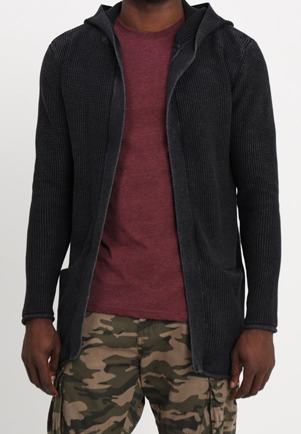 Cardigan noir texturé avec capuche, devant ouvert et deux poches avant, porté sur une chemise bordeaux et un pantalon camouflage.