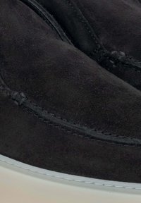 Czarne zamszowe buty o gładkiej fakturze, zaokrąglonym kształcie, kontrastowej białej gumowej podeszwie i subtelnych detalach przeszycia wzdłuż krawędzi.