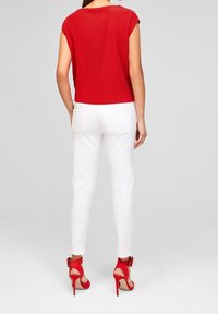 Czerwona plisowana bluzka z krótkimi rękawami, w połączeniu z białymi slim-fit dżinsami i czerwonymi sandałami na wysokim obcasie. Minimalistyczny design, bez wzorów.