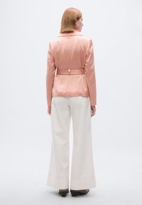 Ροζ ανοιχτόχρωμο σακάκι με ζώνη στη μέση, σε υφή με ανάγλυφο φινίρισμα, σε συνδυασμό με φαρδιά λευκά παντελόνια και καφέ τακούνια.