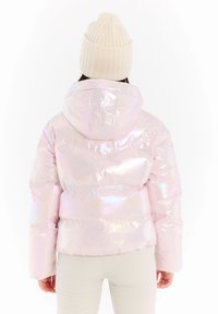 Iridescent pink pufferjakke med hætte, der har et kviltet design og elastisk kant. Personen har en cremefarvet ribbet hue på.
