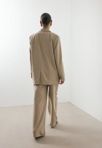 Traje beige ajustado con una chaqueta estructurada y pantalones de pierna ancha, con sutiles detalles de costura y una textura de tela suave.