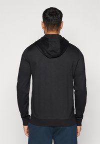 Sweatshirt nero con cappuccio, dalla texture liscia, maniche aderenti e orlo a coste. Nessun motivo o elemento hardware evidente.